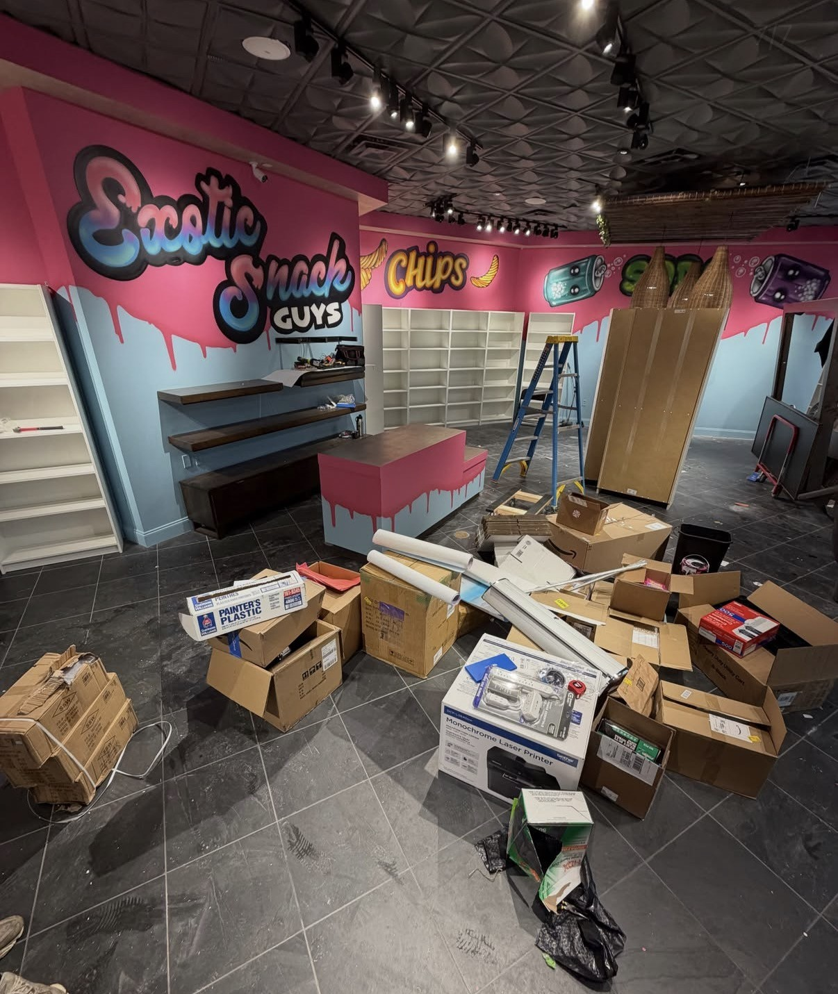 Retail store interior being fitted out with shelves, counter, and packing boxes awaiting removal